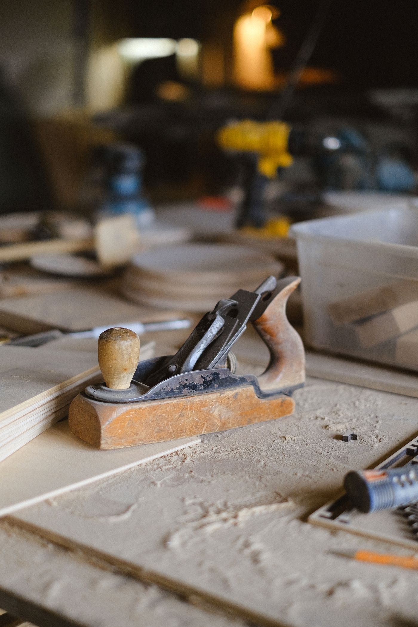 A wooden hand plane resting on a sawdust-covered bench, tools and offcuts behind it