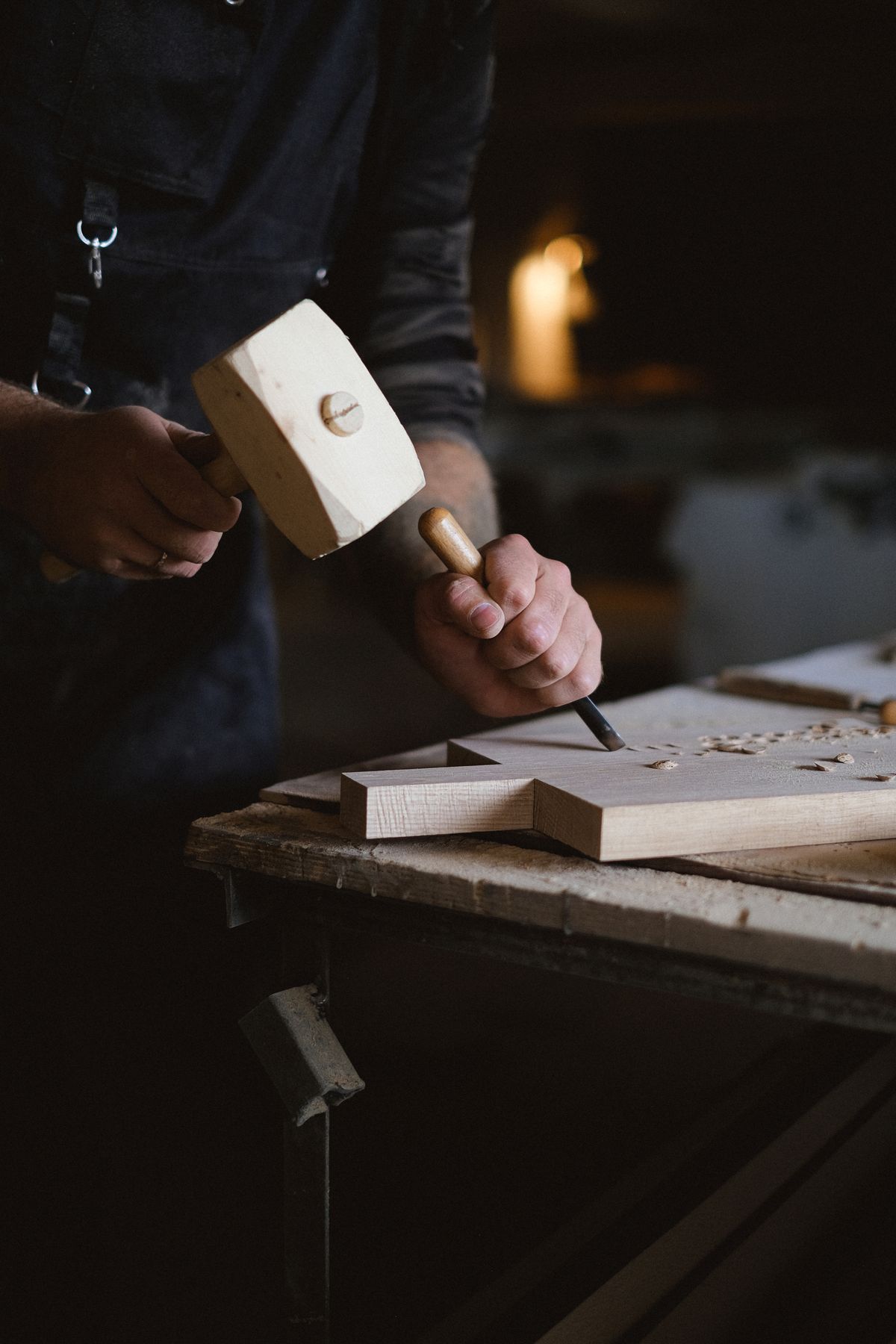 A joiner driving a chisel with a wooden mallet, chopping a mortise in an oak rail