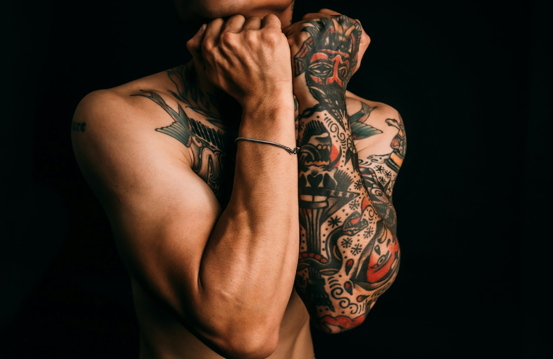 Crossed forearms sleeved in traditional tattoo work, black and red, against a black background