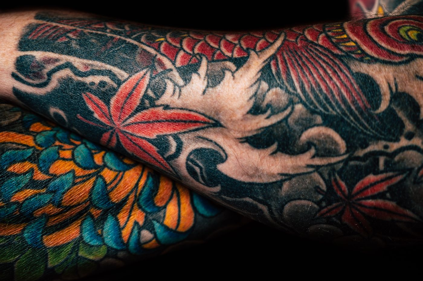Close-up of a colour leg piece: a red koi, maple leaves and a chrysanthemum over black wave work