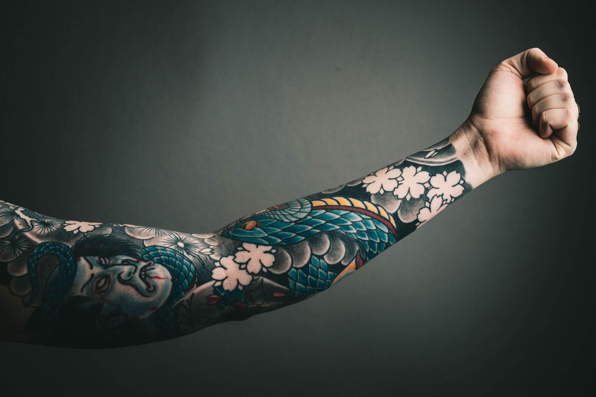 A Japanese sleeve of a serpent, cherry blossoms and waves on a dark ground