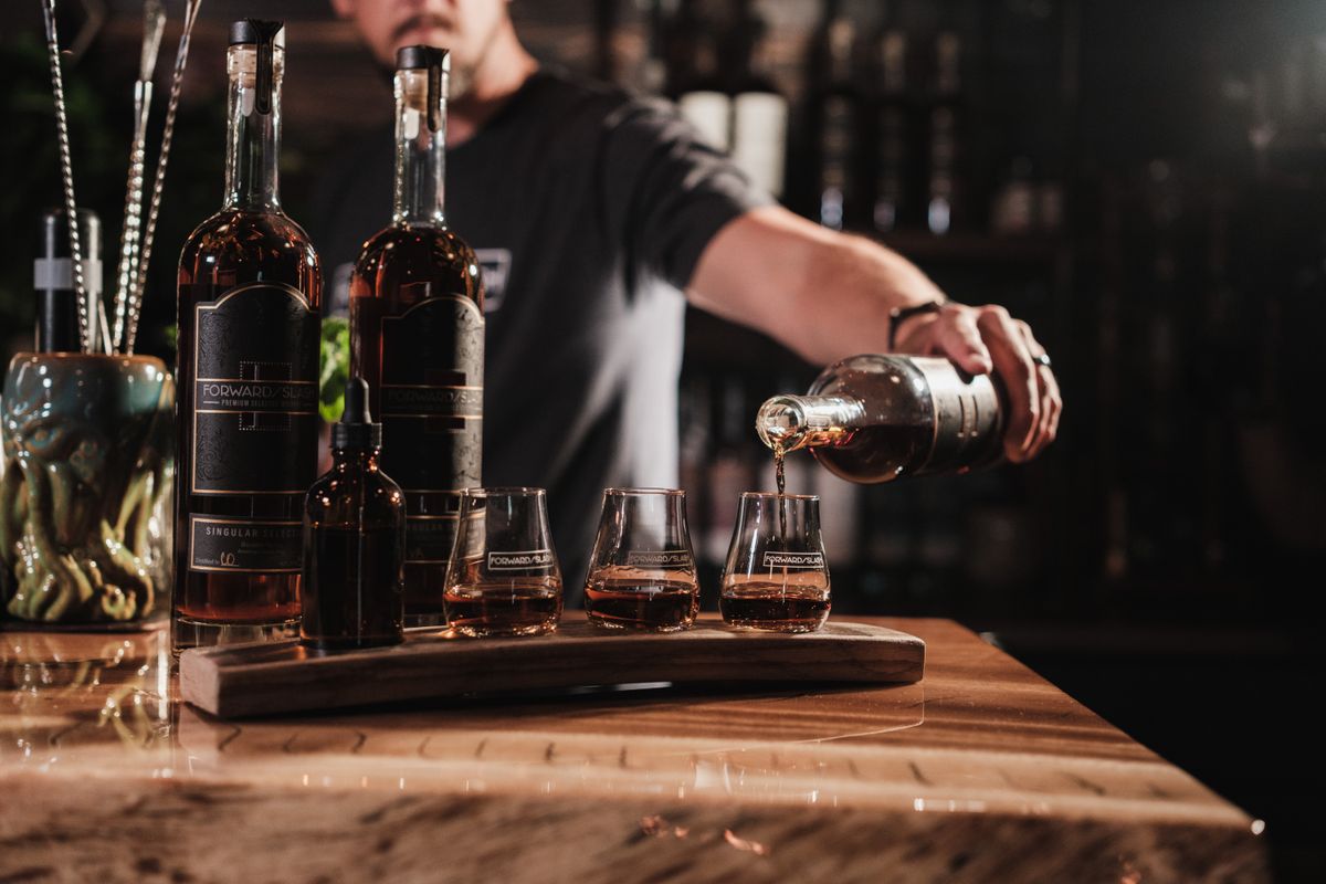 A tasting flight being poured across four glasses on a wooden board at the bar