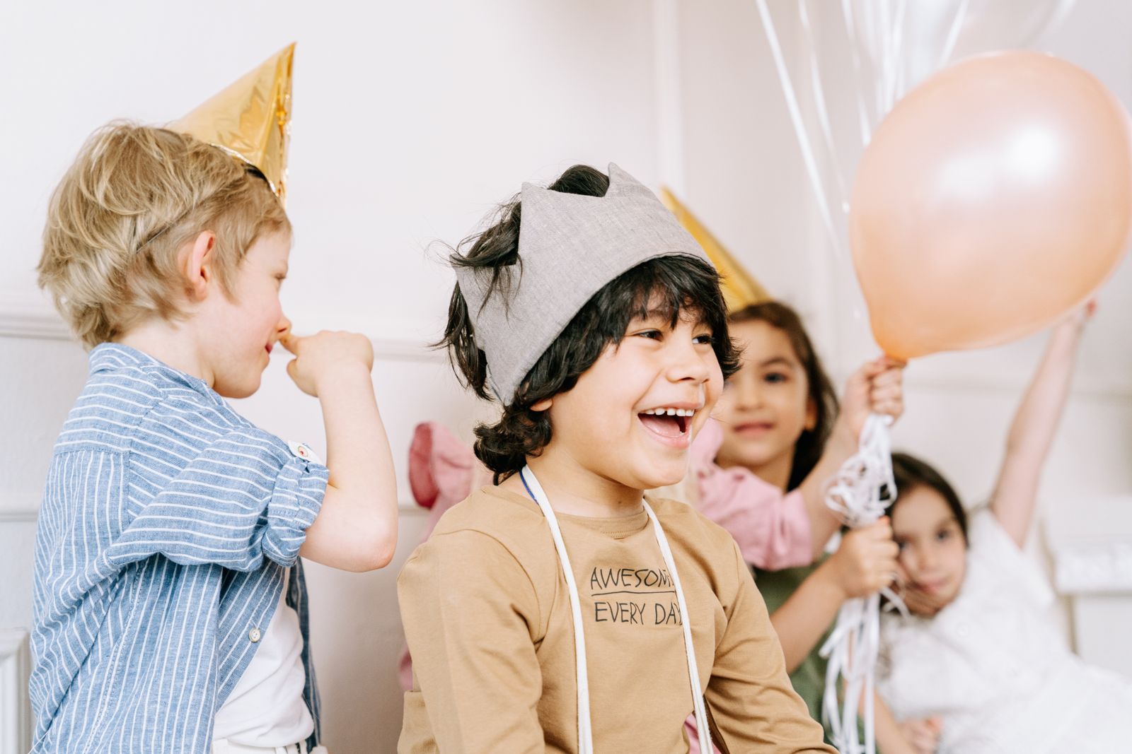 Children in party hats laughing around a table of balloons