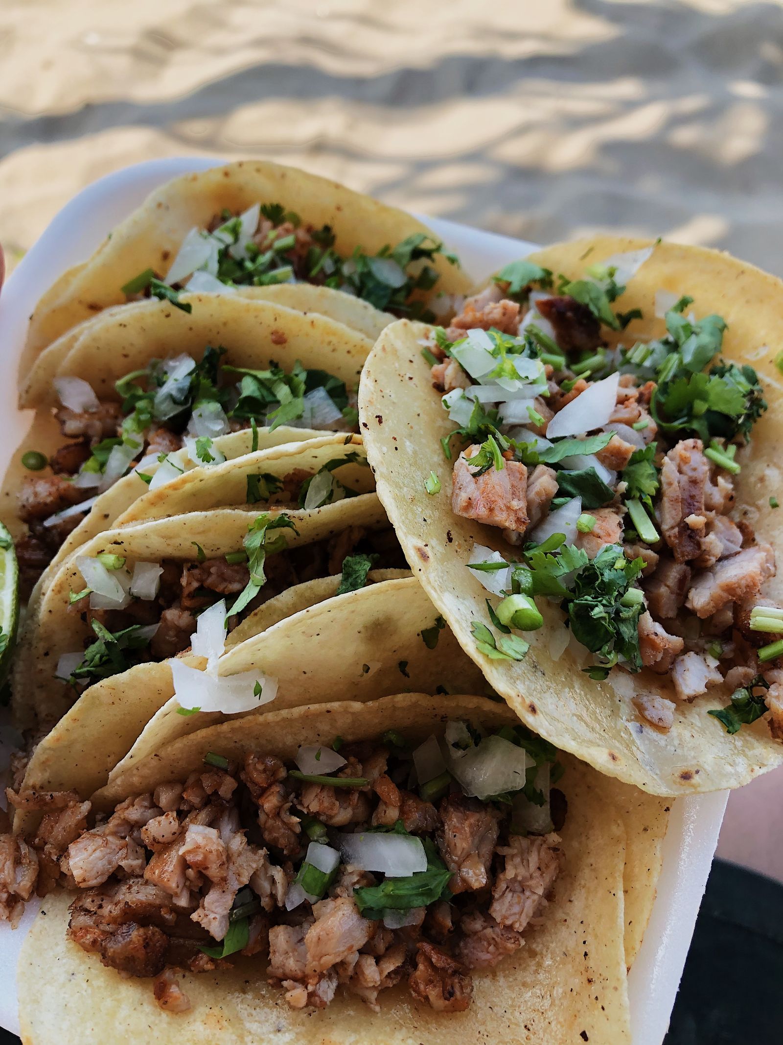 Three tacos on corn tortillas piled with meat, onion and cilantro