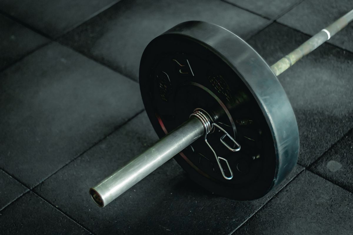 A loaded barbell resting on rubber flooring, bumper plate and collar in close focus