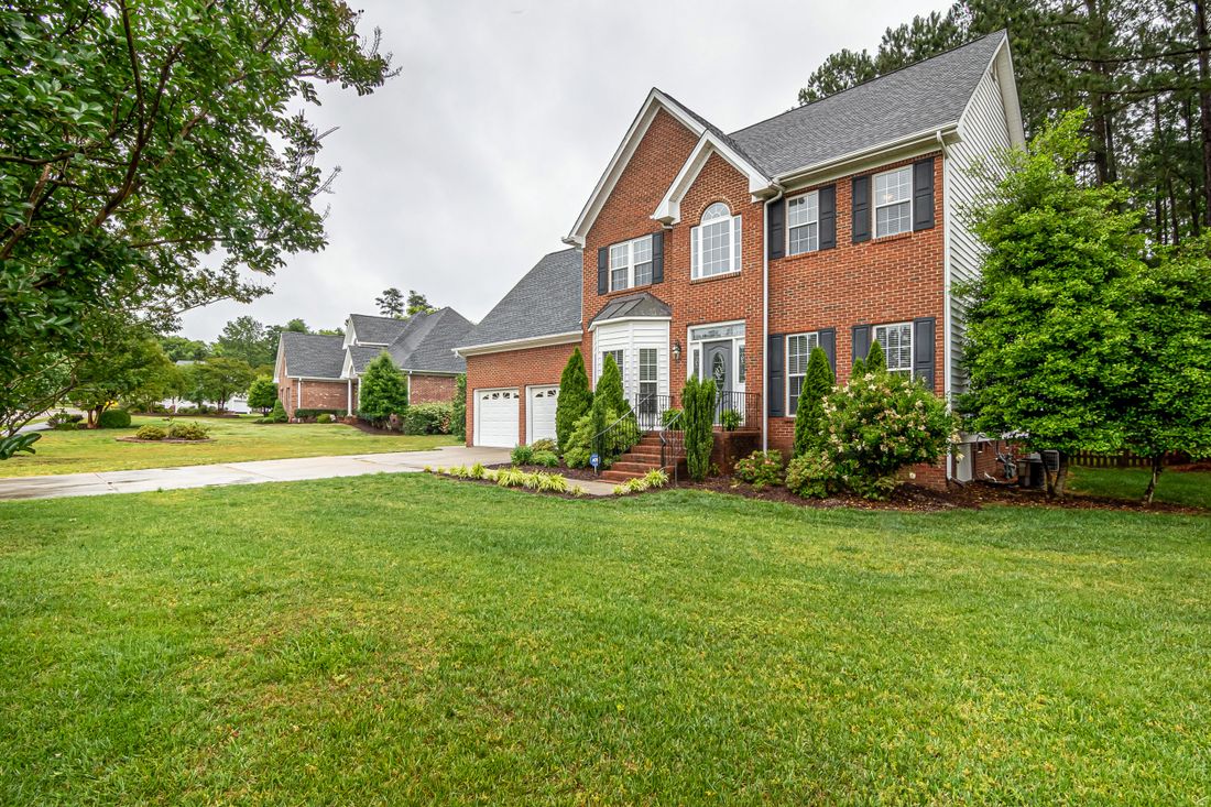 A brick house with a wide, evenly cut front lawn and edged beds along the drive