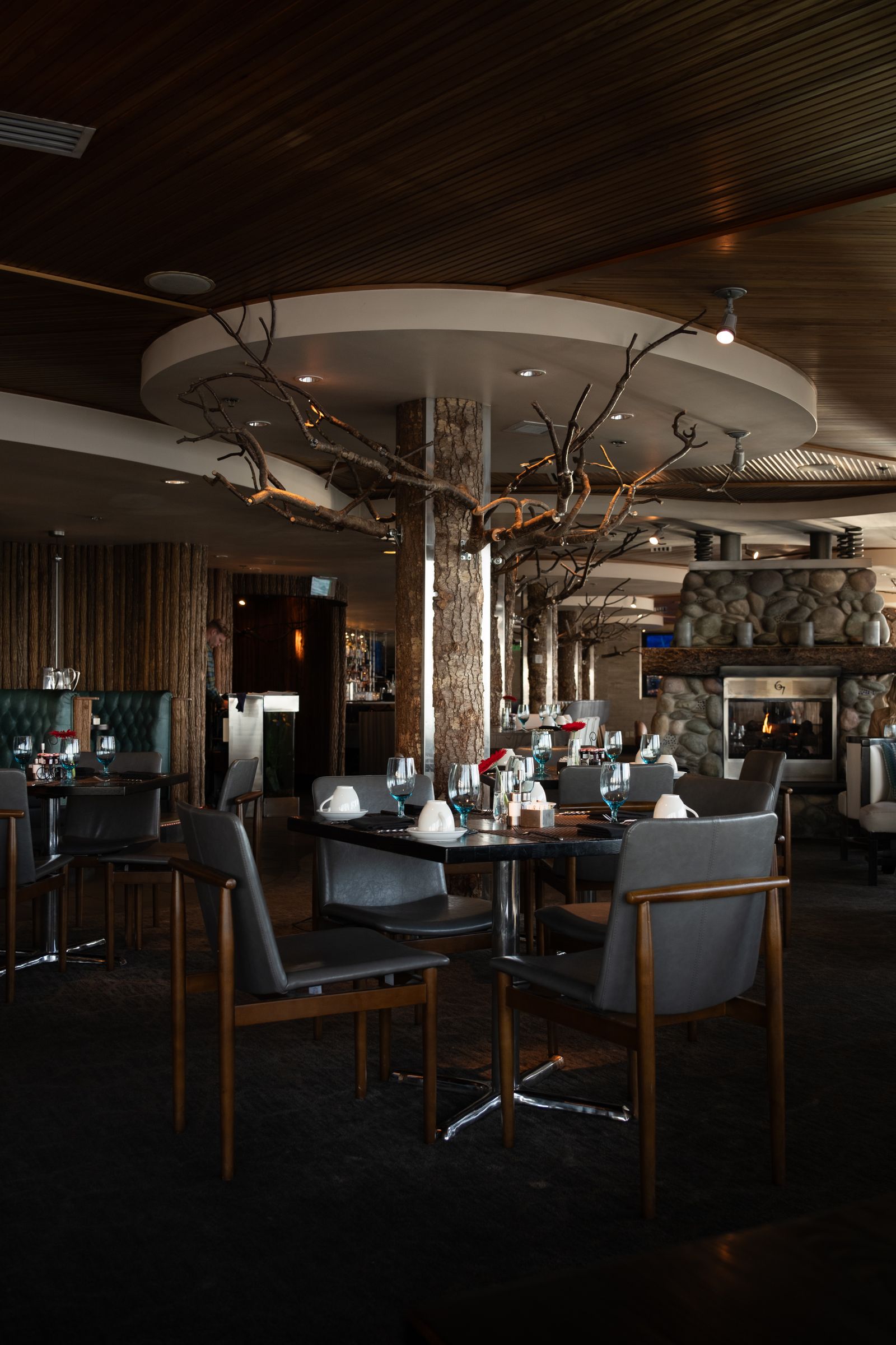 The dining room at dusk: wooden tables, low warm light and a lit hearth
