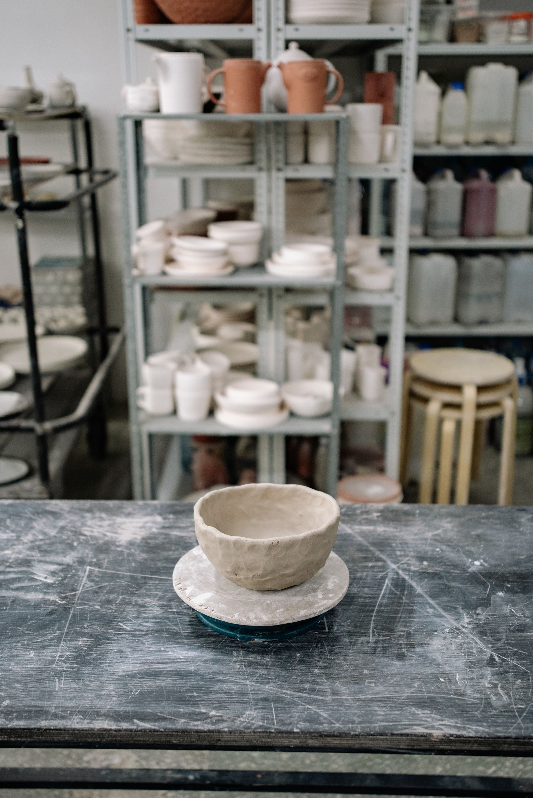 A hand-thrown ceramic bowl on the workshop table, still unglazed, with shaping tools beside it