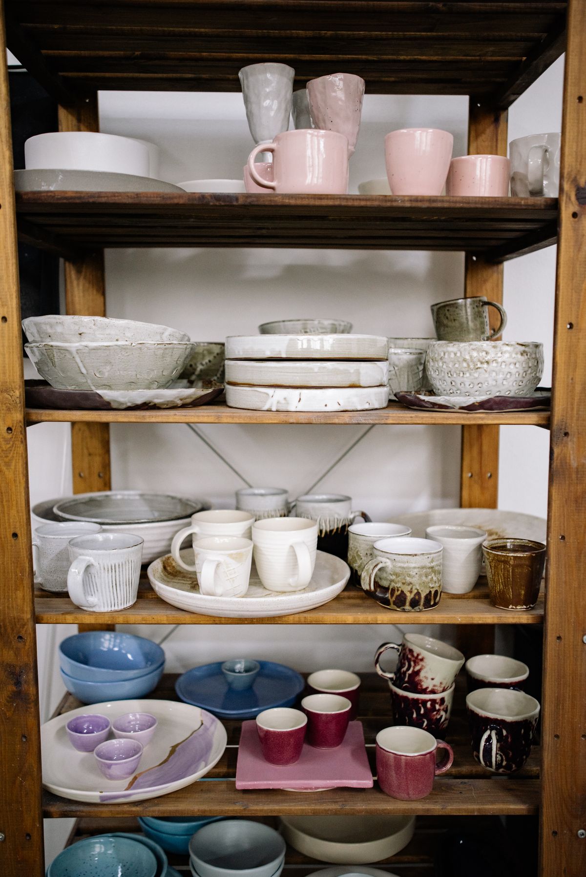 Rows of finished mugs and small bowls on the studio shelves