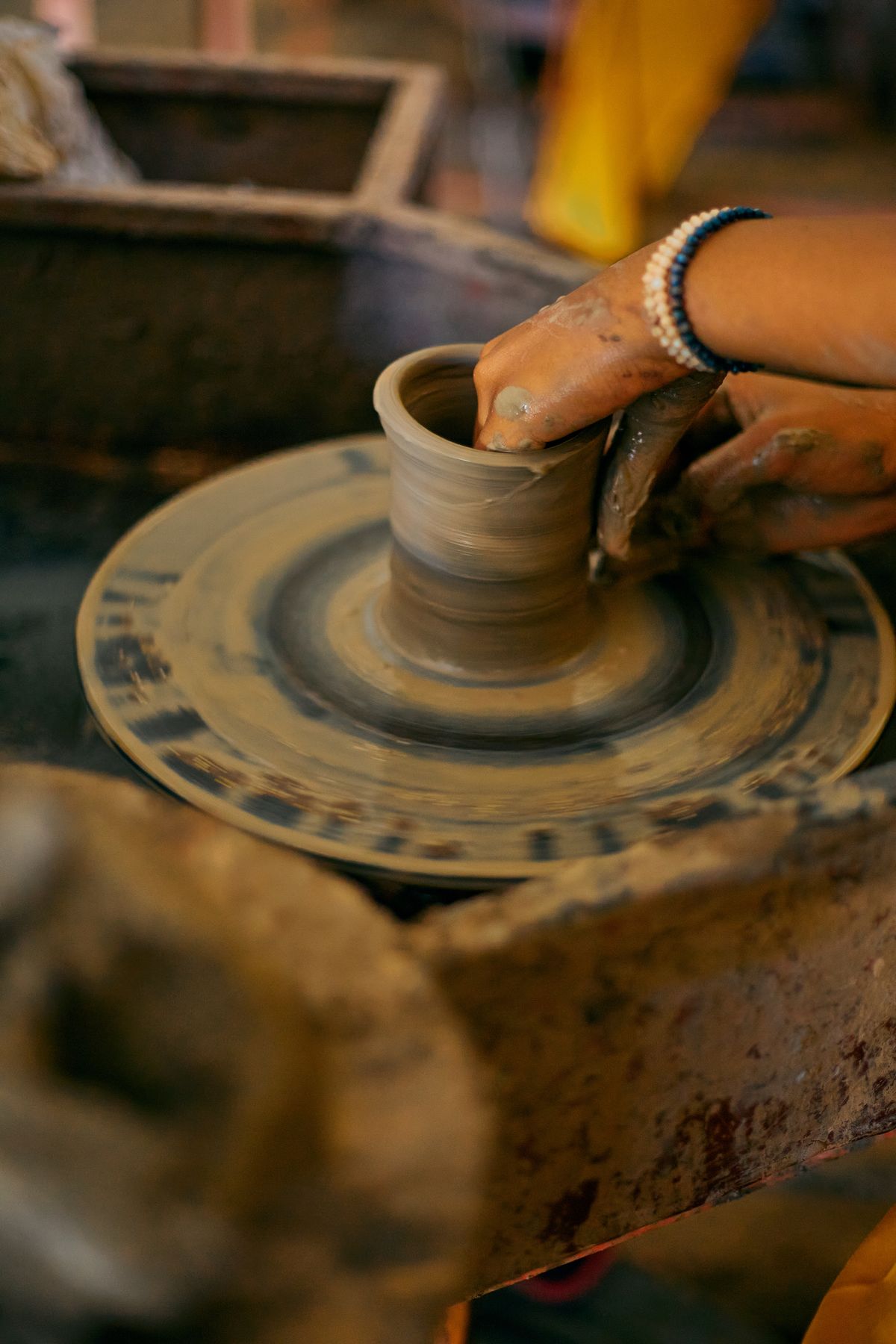 Two hands centring clay on a spinning pottery wheel under warm light
