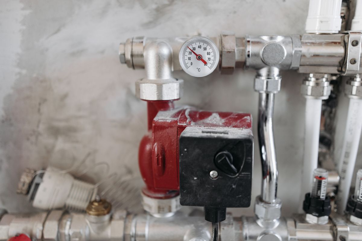 A heating manifold with pressure gauge, circulator pump and copper runs on a basement wall
