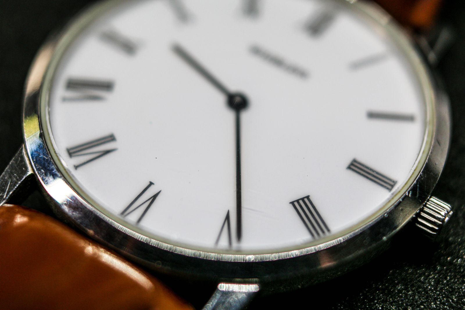 Extreme close-up of a silver watch dial with Roman numerals and slender hands