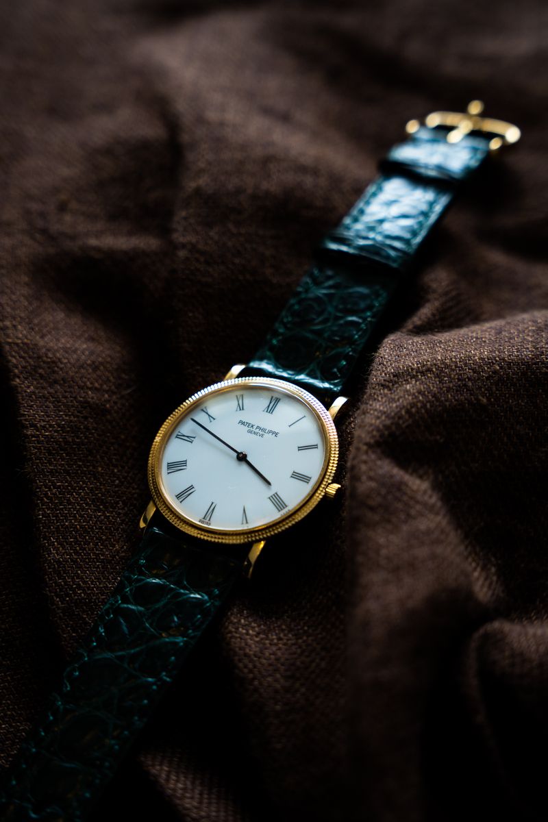 Patek Philippe Calatrava in yellow gold on a dark crocodile strap, white dial, resting on brown cloth