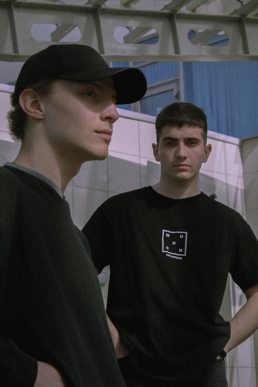 A figure in a plain black six-panel cap and black tee, shot in cold daylight