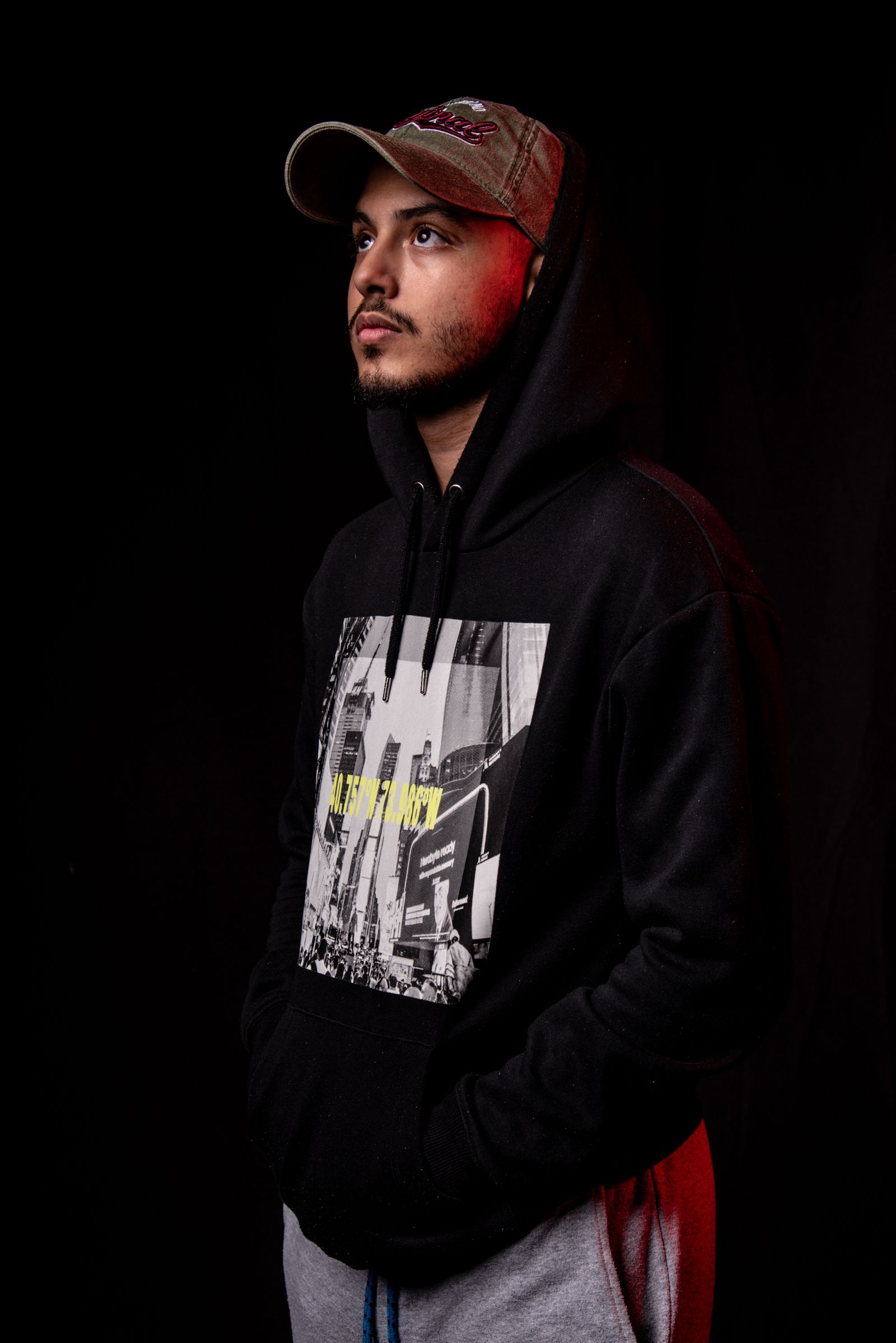 A figure in a black hoodie and cap shot against a dark studio backdrop