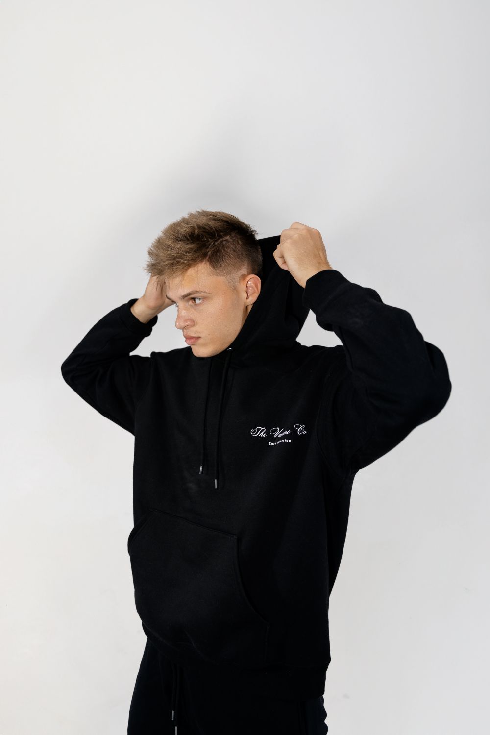 A figure pulling up the hood of a heavyweight black hoodie