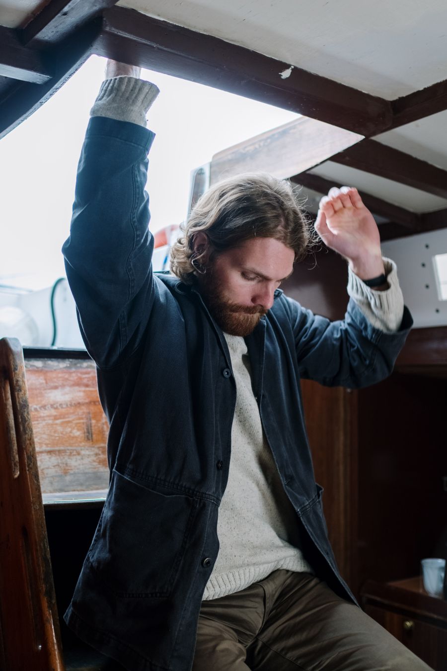 A worn dark chore coat over a cream knit, snap placket and patch pockets, shot in daylight
