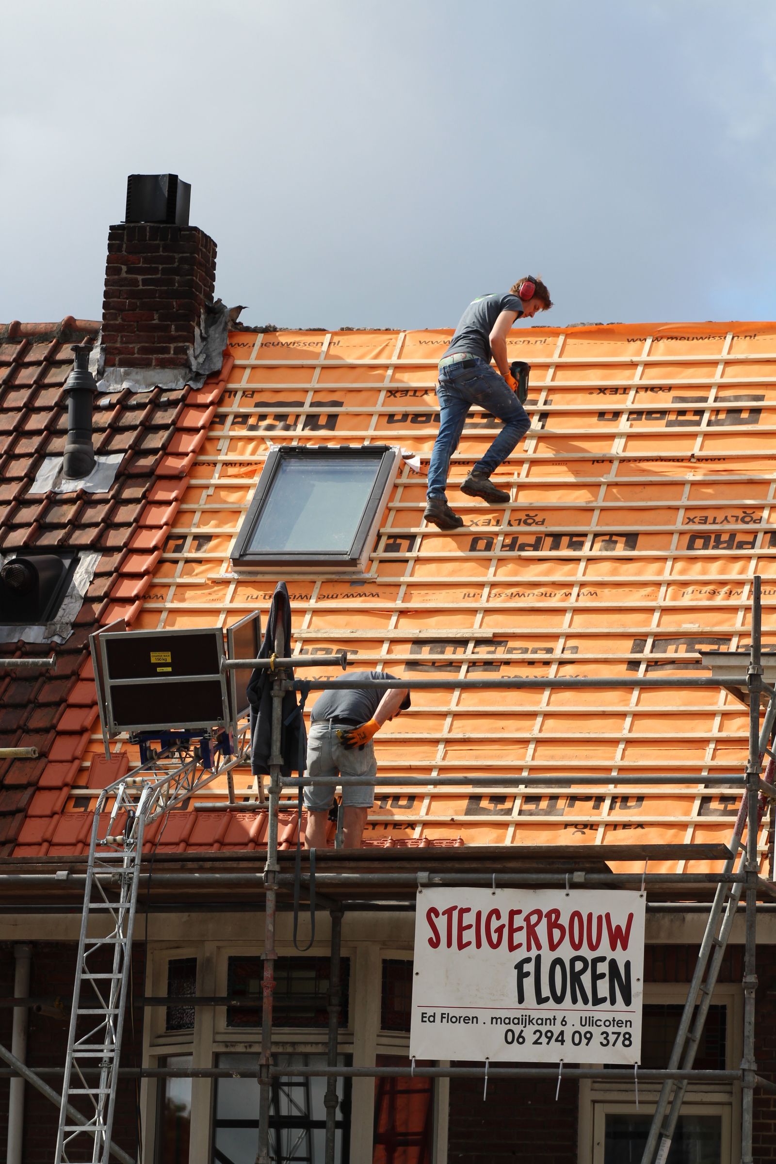 Two roofers working across a pitched roof against a clear sky