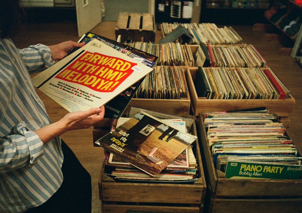 Hands pulling a sleeve from a wooden crate of second-hand records at the shop counter