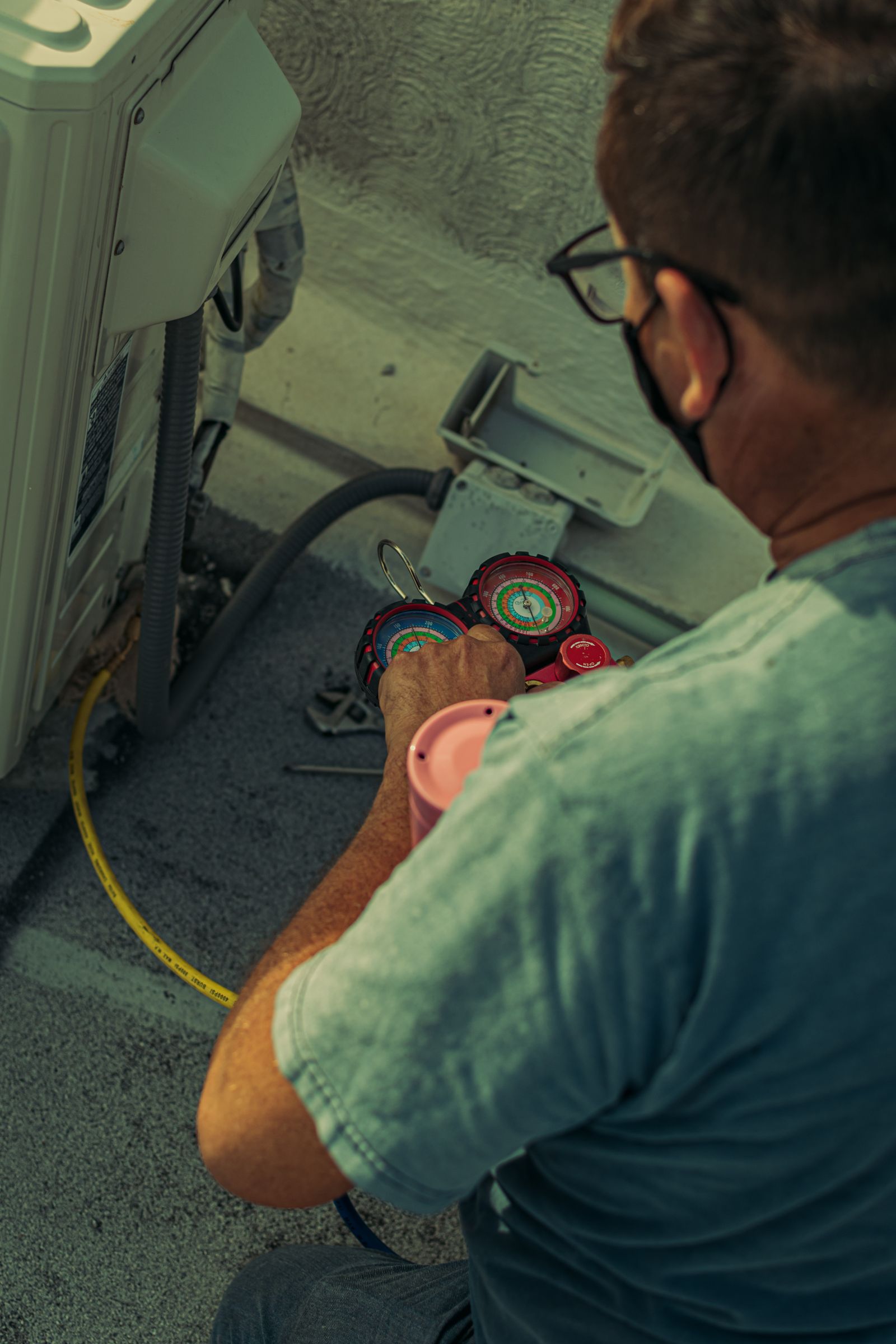 A technician checking refrigerant pressures on an outdoor condenser with manifold gauges