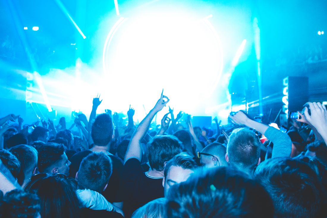 A packed dance floor lit blue, hands up toward the lighting rig.
