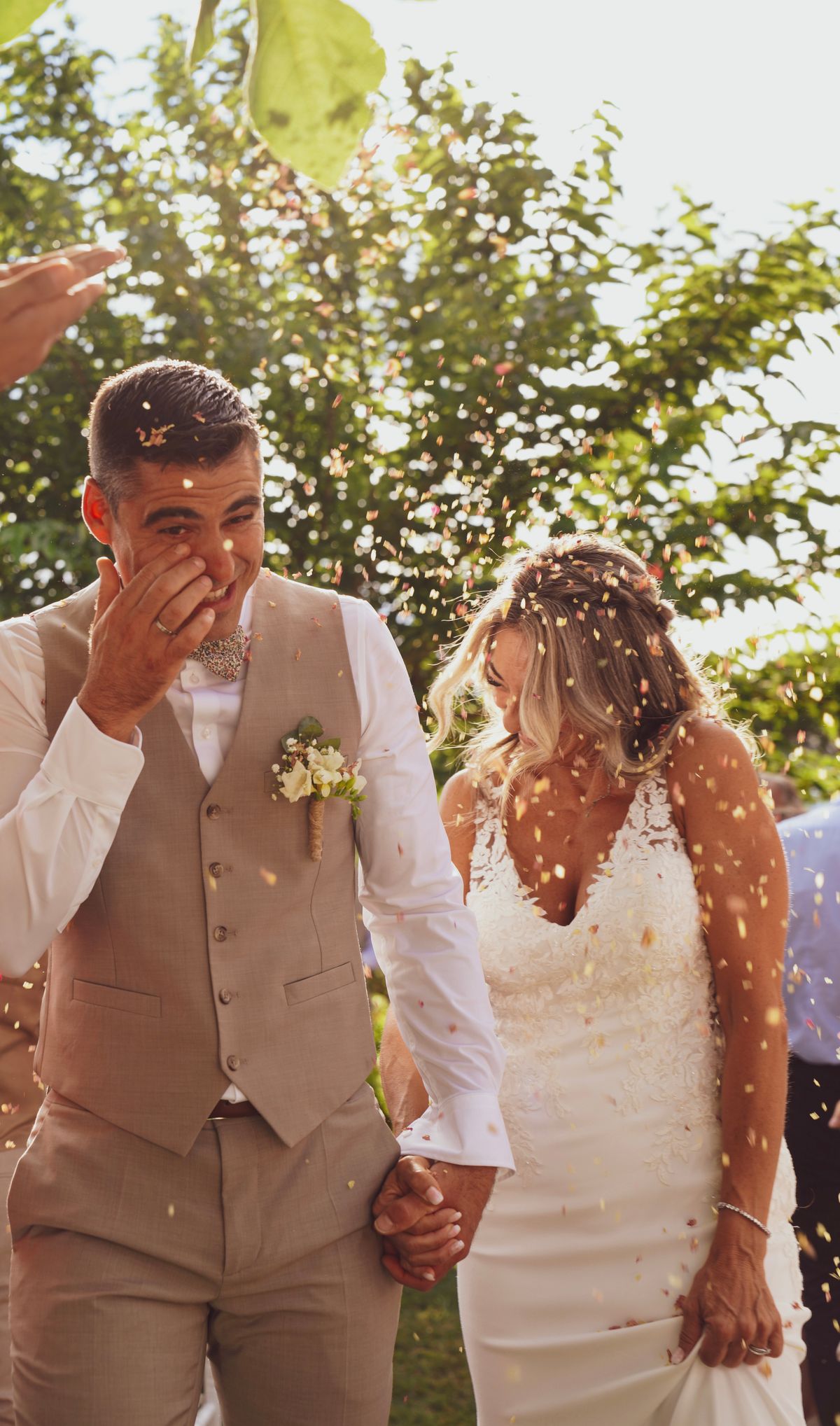 A couple laughing, hand in hand, walking through a shower of confetti in golden afternoon light