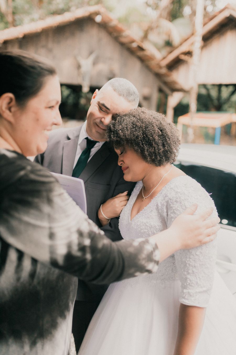 A couple leaning together, heads bowed, while the officiant's hand rests on the bride's shoulder