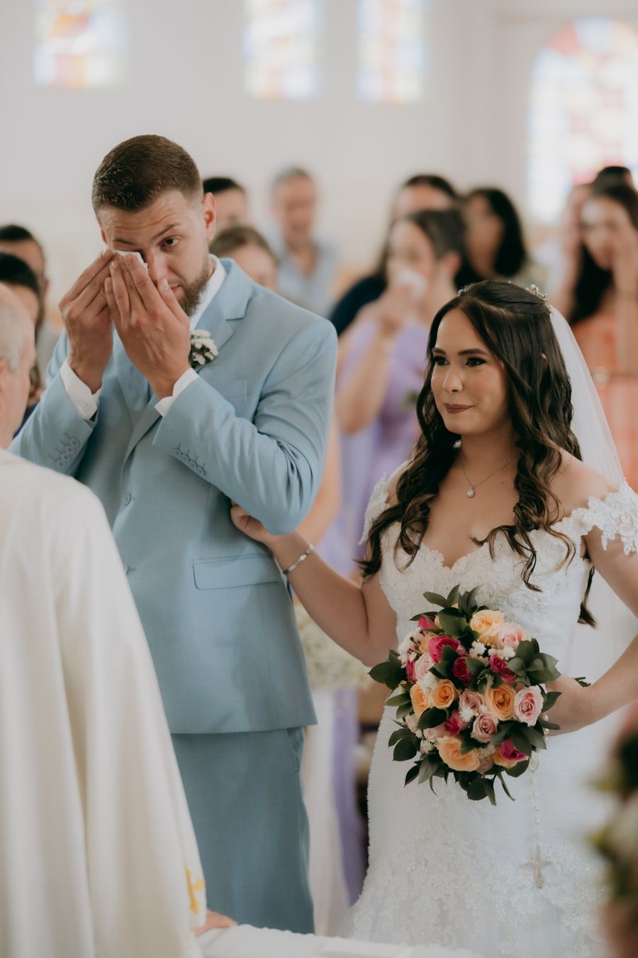 A groom wiping his eyes at the altar while the bride holds his arm